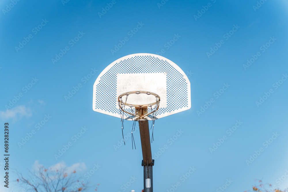 Basketball basket seen from below and from the front while an orange ball is falling from above. Contrasted with a blue sky on a sunny, clear day. Basketball basket seen from below and from the front while an orange ball is falling from above. Contrasted with a blue sky on a sunny, clear day.