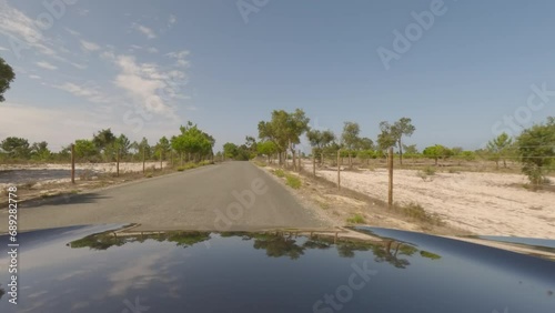 First person view, FPV, from dashcam of car driving along the Alentejo Coast in Portugal, passing cork oak trees and sand dunes. Road trip video in POV, with blue sky on an empty road photo