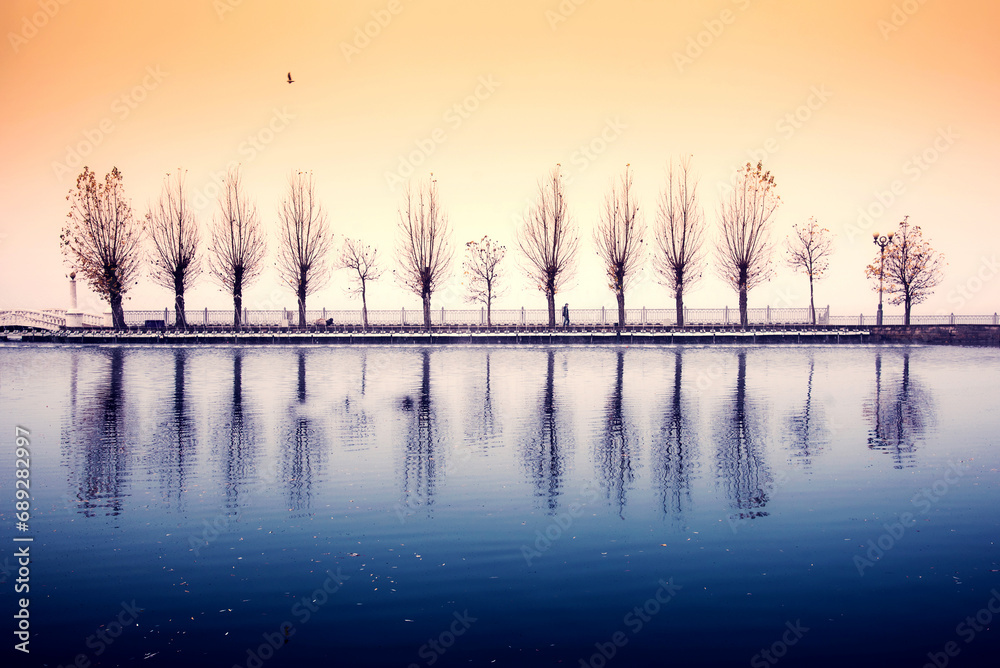 Mystical spooky depressing autumn landscape with a lonely silhouette of a passerby on a background of fog over the lake. (Autumn depression, sadness, psychotherapy - concept)
