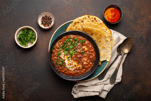 Traditional Indian Punjabi dish Dal makhani with lentils and beans in black bowl served with naan flat bread, fresh cilantro and two spoons on brown concrete rustic table top view. photo