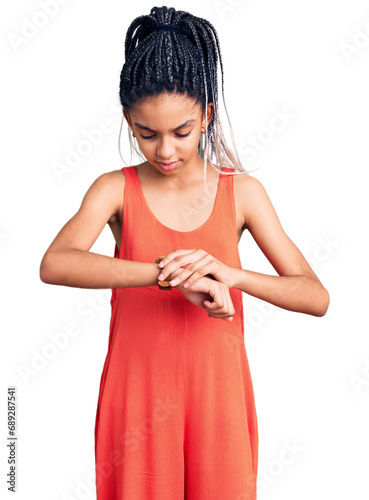 Cute african american girl wearing casual clothes checking the time on wrist watch, relaxed and confident © Krakenimages.com