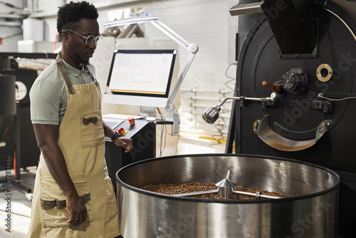 Portrait of African American young man watching coffee roasting process and operating machines  copy space