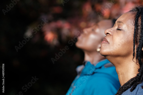 Two black mature women relaxed with closed eyes outdoors.