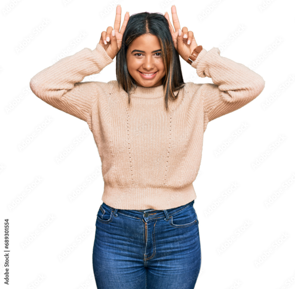 Young latin girl wearing wool winter sweater posing funny and crazy with fingers on head as bunny ears, smiling cheerful Young latin girl wearing wool winter sweater posing funny and crazy with fingers on head as bunny ears, smiling cheerful