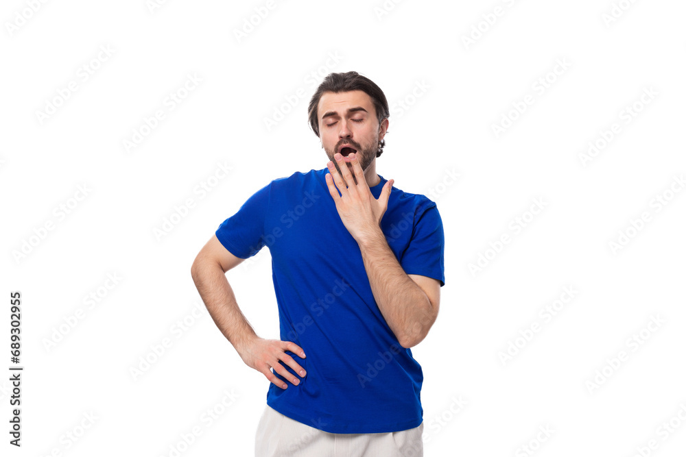 young brunette man with a beard dressed in a blue T-shirt yawns on a white background young brunette man with a beard dressed in a blue T-shirt yawns on a white background