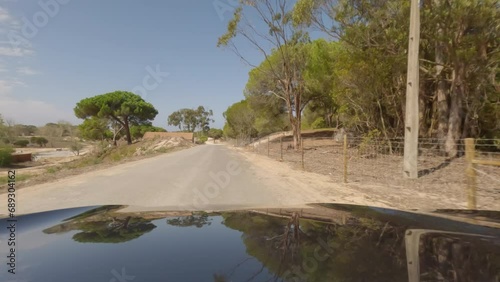 First person view, FPV, from dashcam of car driving along the Alentejo Coast in Portugal towards beach, passing cork oak trees and sand dunes. Road trip video in POV, with blue sky on an empty road photo