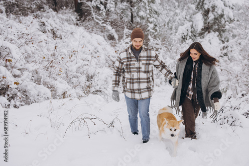 Happy young couple with akita dog in forest on winter and snowly day