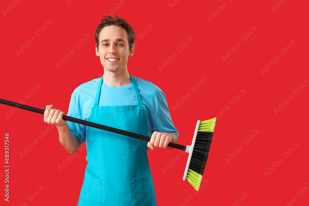 Male janitor with broom on red background