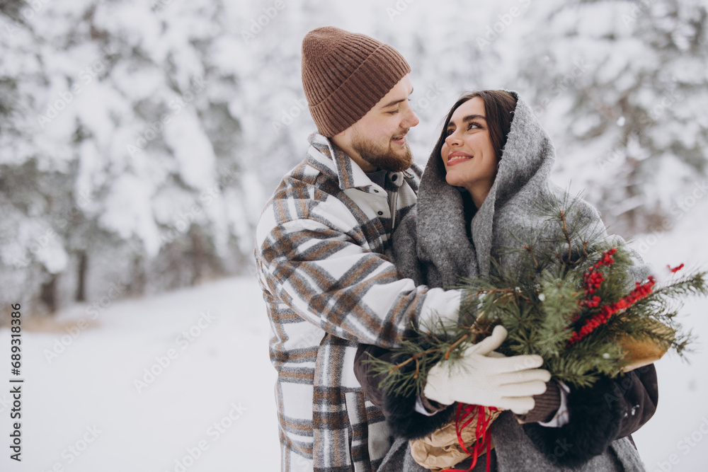 Cute young couple in love with pine bouquet spending time on Valentine's day in snowy winter forest in mountains