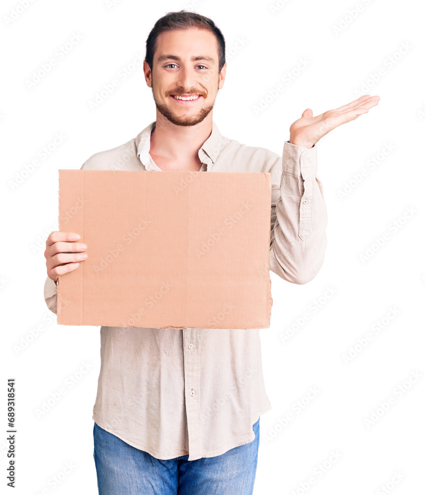 Young handsome caucasian man holding empty cardboard banner celebrating victory with happy smile and winner expression with raised hands Young handsome caucasian man holding empty cardboard banner celebrating victory with happy smile and winner expression with raised hands
