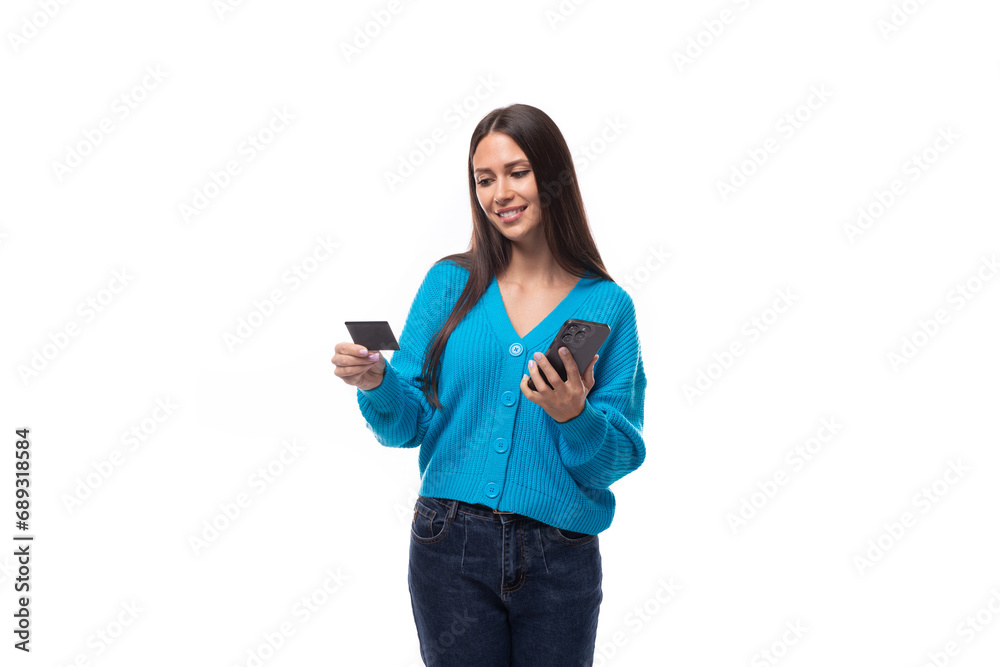confused young brunette woman dressed in a blue sweater with buttons holds a bank card and a smartphone. e-business concept confused young brunette woman dressed in a blue sweater with buttons holds a bank card and a smartphone. e-business concept