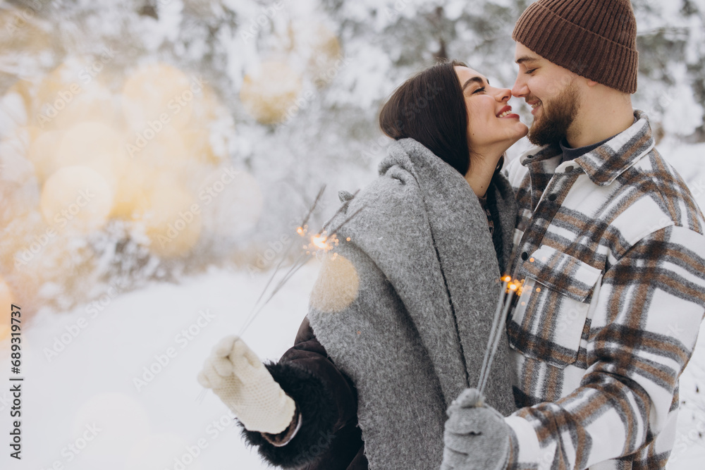 Happy romantic couple in love holding sparklers in snowy winter forest Happy romantic couple in love holding sparklers in snowy winter forest