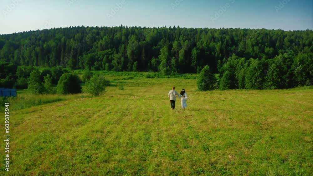 Young boy and girl in ethnic outfits running through a green field in the early morning, holding hands. The girl is wearing a flower wreath and a white dress, the young man is wearing a linen shirt Young boy and girl in ethnic outfits running through a green field in the early morning, holding hands. The girl is wearing a flower wreath and a white dress, the young man is wearing a linen shirt