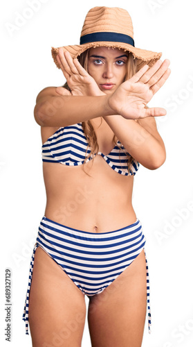 Young beautiful blonde woman wearing bikini and hat rejection expression crossing arms doing negative sign, angry face