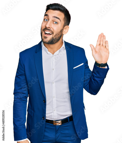 Young hispanic man wearing business jacket waiving saying hello happy and smiling, friendly welcome gesture