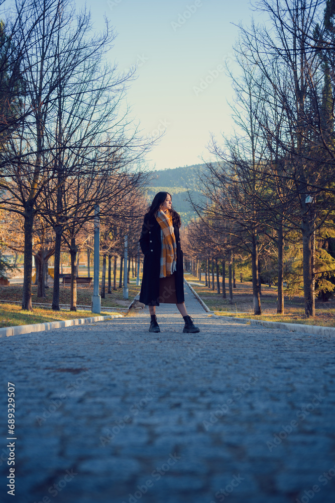 Woman in an overcoat and scarf walks through an autumn park at dusk Woman in an overcoat and scarf walks through an autumn park at dusk