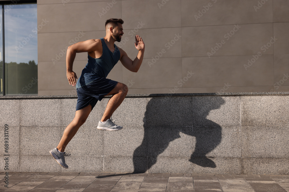 Fototapeta premium Young man running near building outdoors. Space for text