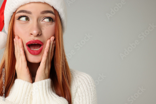Young woman in Santa hat on light grey background, space for text. Christmas celebration