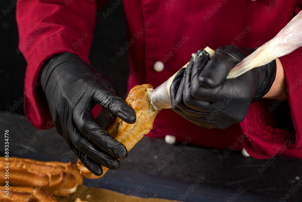 Chef Fills freshly baked eclairs with custard using a cooking pouch while pouring custard into the eclairs Chef Fills freshly baked eclairs with custard using a cooking pouch while pouring custard into the eclairs