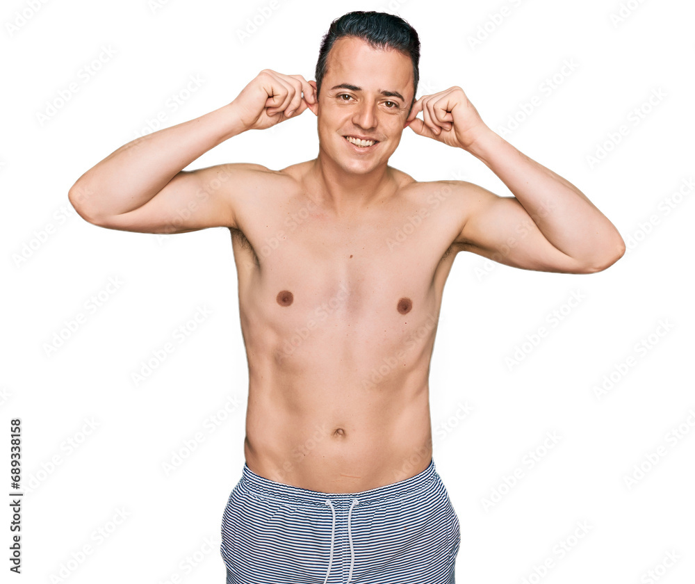 Handsome young man wearing swimwear shirtless smiling pulling ears with fingers, funny gesture. audition problem Handsome young man wearing swimwear shirtless smiling pulling ears with fingers, funny gesture. audition problem