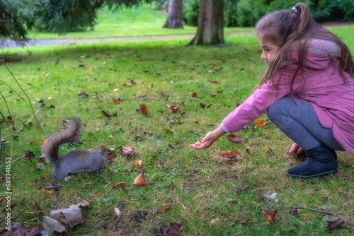 Young girl feeding from hand Grey Squirrel, Latin name Sciurus Carolinensis, with some peanuts in the park, Botanic Garden, Dublin, Ireland