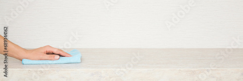 Obraz na plátně Young adult woman hand holding blue dry rag and wiping beige stone tabletop at home kitchen