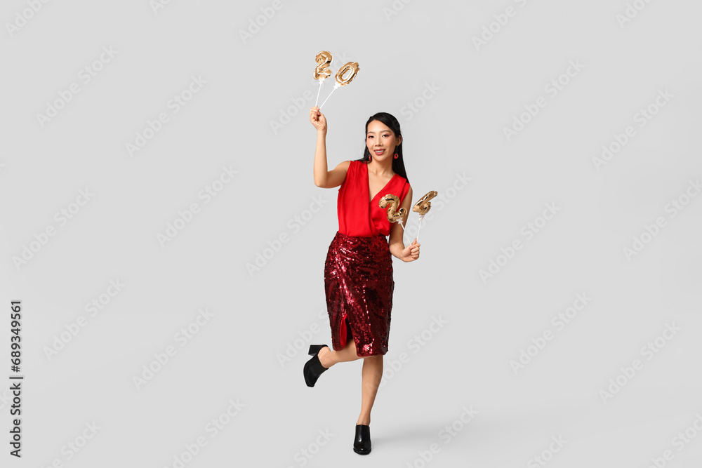 Beautiful young happy Asian woman with figure 2024 made of balloons on grey background. Chinese New Year celebration