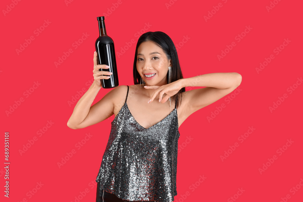 Beautiful Asian woman with bottle of wine on red background Beautiful Asian woman with bottle of wine on red background