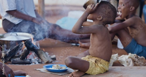 Poor, malnourished Black African child due to extreme poverty, drought and climate change. Drinking water from a cooking pot photo