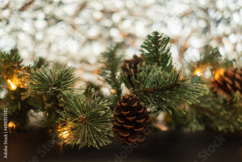 horizontal photograph. A green branch with a New Year's garland shines against the background of crumpled foil. Decorated with a pine cone. Place for text, gift card. Christmas mood