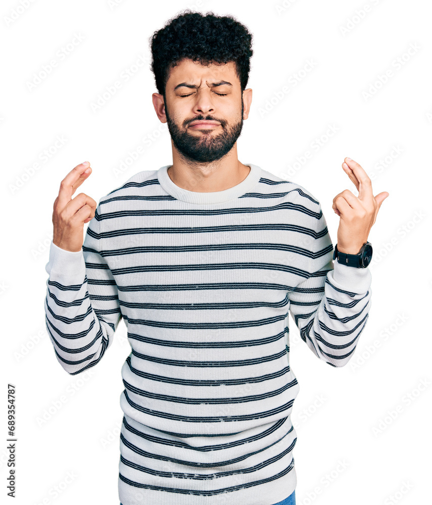 Fototapeta premium Young arab man with beard wearing casual striped sweater gesturing finger crossed smiling with hope and eyes closed. luck and superstitious concept.
