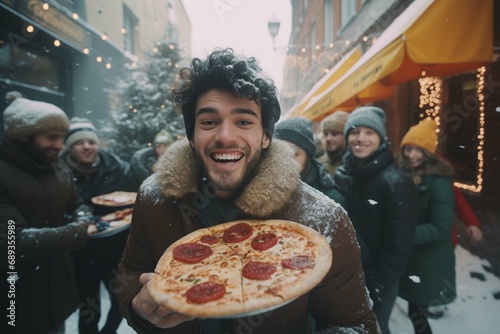 A happy young man with take-out pizza in his hands for a large group of friends in winter on the veranda of a cafe.