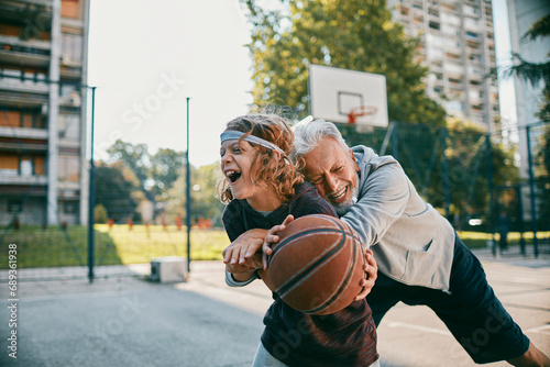 Smiling grandfather having fun with grandson on basketball court