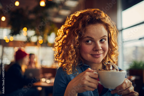 Young woman enjoying cup of whipped cream topped coffee in cafe photo