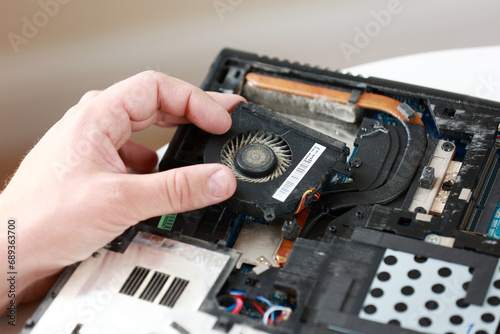 Fixing laptop. Repairman holds cooling fan and repairs from overheating. Disassembling computer, replacement, clean dust and dirt cooling system on notebook. Professional electronic device service