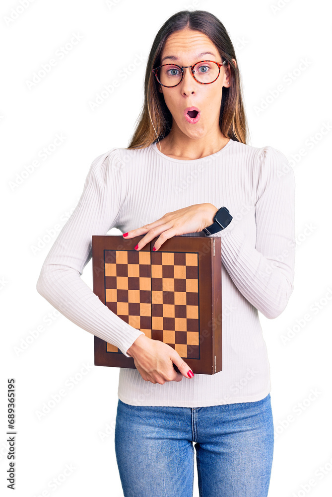 Beautiful brunette young woman holding chess scared and amazed with open mouth for surprise, disbelief face Beautiful brunette young woman holding chess scared and amazed with open mouth for surprise, disbelief face