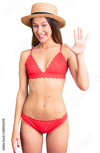 Beautiful brunette young woman wearing bikini showing and pointing up with fingers number five while smiling confident and happy.