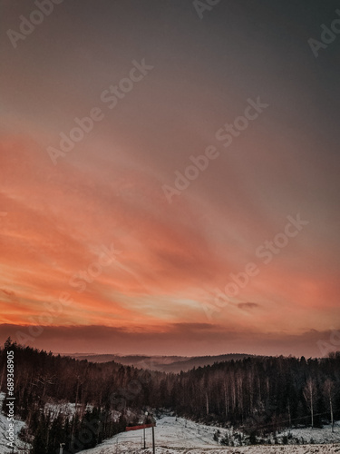Tranquil winter sunset over snowy mountain landscape with coniferous trees.