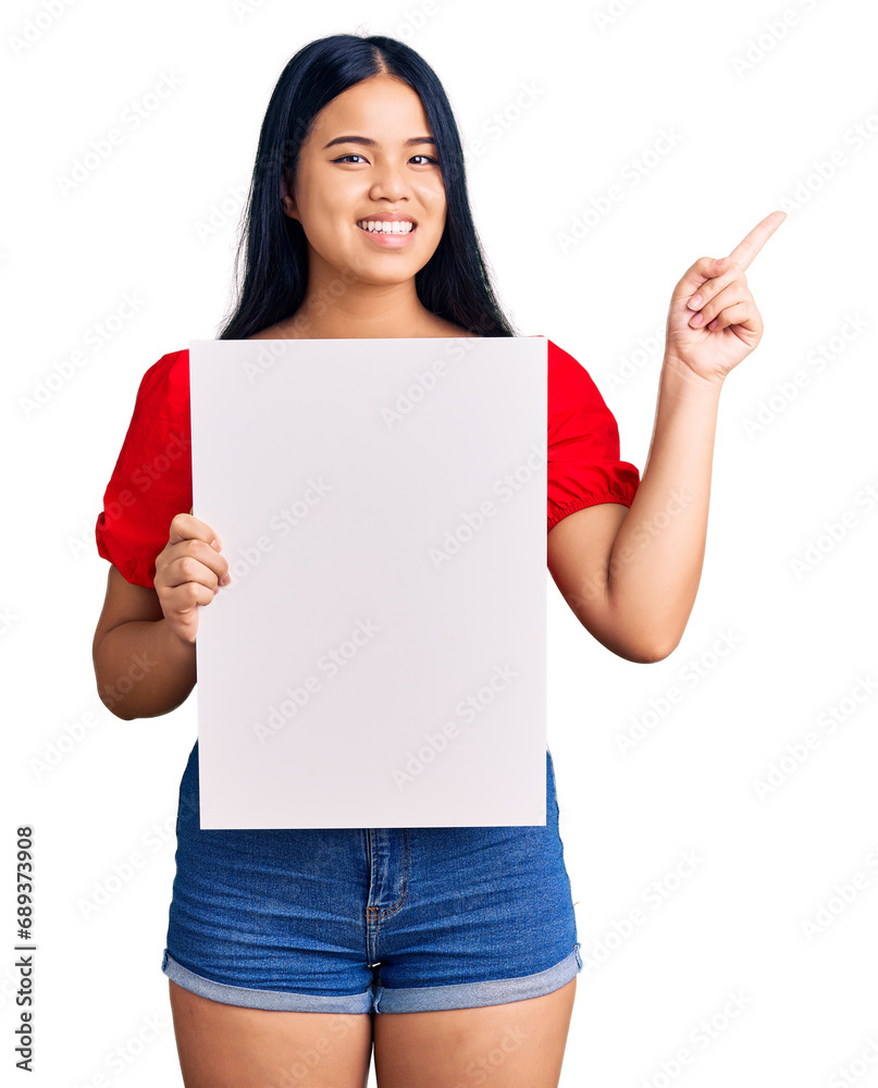 Young beautiful asian girl holding blank empty banner smiling happy pointing with hand and finger to the side Young beautiful asian girl holding blank empty banner smiling happy pointing with hand and finger to the side