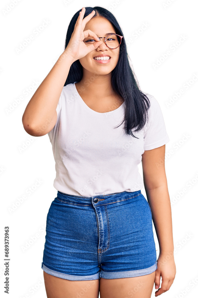 Young beautiful asian girl wearing casual clothes and glasses doing ok gesture with hand smiling, eye looking through fingers with happy face.