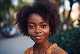 Portrait of charming african american young woman with curly hair smiling and looking at camera outdoors