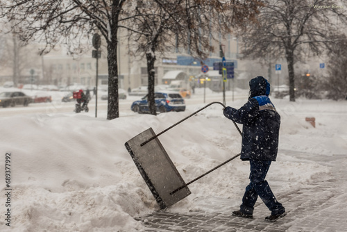 Fotografie A labouring man shoveling away snow in Moscow, struggling with big banks of snow