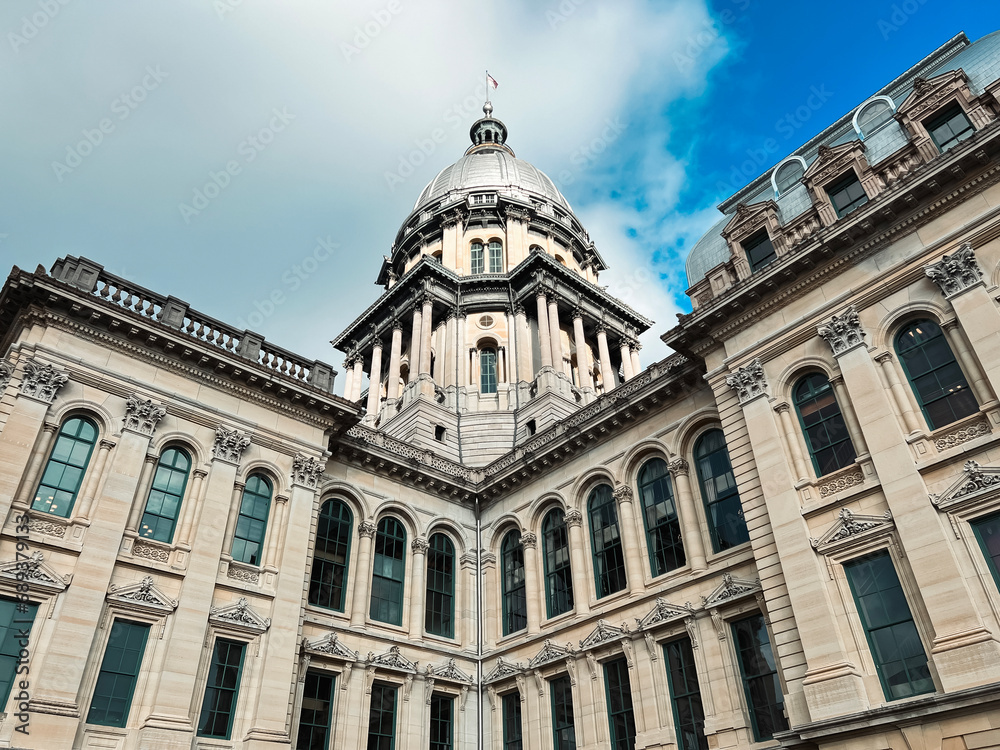 Rear views of the Illinois State Capitol Building in Springfield, Illinois, USA. Cloudy blue skies overhead. Sunlight shines down upon the dome of the building.