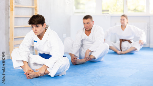 Woman and man in kimono sits in a butterfly pose and practices stretching in sport gym