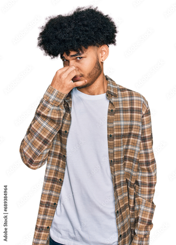 Young african american man with afro hair wearing casual clothes smelling something stinky and disgusting, intolerable smell, holding breath with fingers on nose. bad smell Young african american man with afro hair wearing casual clothes smelling something stinky and disgusting, intolerable smell, holding breath with fingers on nose. bad smell