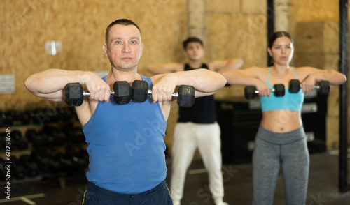 Dedicated man doing exercises with dumbbells near other people in gym