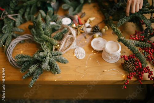 Woman making Christmas wreath using natural pine branches, sitting near wooden table.