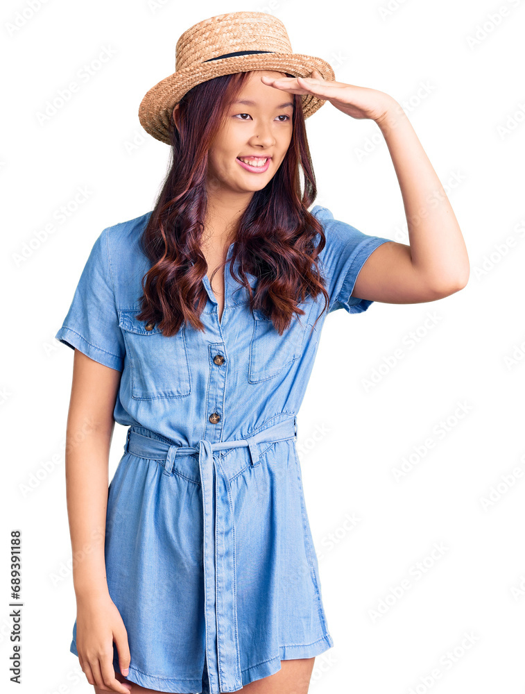 Young beautiful chinese girl wearing summer hat very happy and smiling looking far away with hand over head. searching concept. Young beautiful chinese girl wearing summer hat very happy and smiling looking far away with hand over head. searching concept.
