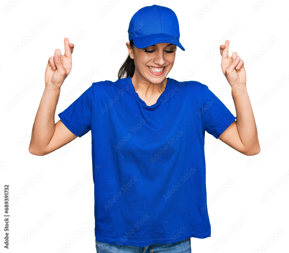 Young hispanic girl wearing delivery courier uniform gesturing finger crossed smiling with hope and eyes closed. luck and superstitious concept.