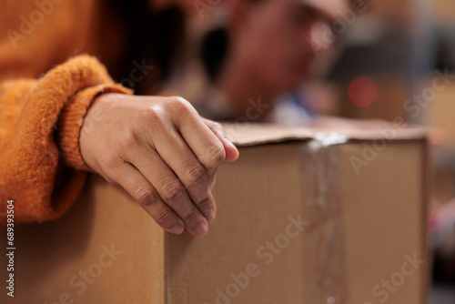 Package handler arm holding packed cardboard box in industrial warehouse. Storehouse employee picking order and preparing customer parcel for transportation with close up on worker hand photo